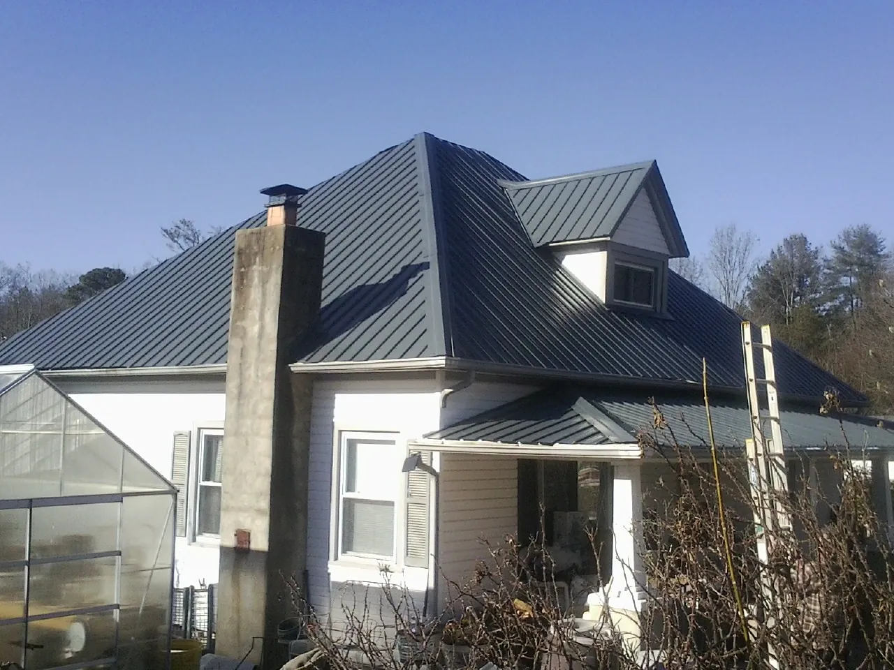 Dark blue standing seam metal roof on a white farmhouse with dormer — Slate & Tile Roof Repair by Roofing Brothers in Sagle