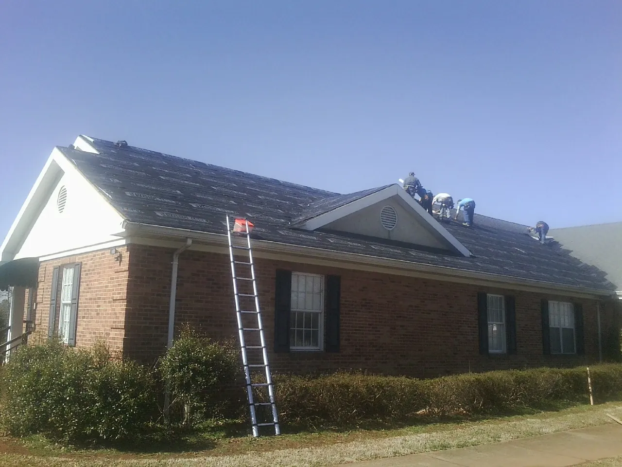 Crew tearing shingles off a brick ranch roof with a ladder set — Metal Roof Repair work by our crew in Sagle