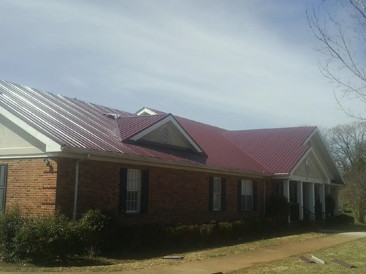 Red metal roof with gabled entries on a long brick building, from a Hail Damage Roof Repair job in Sagle