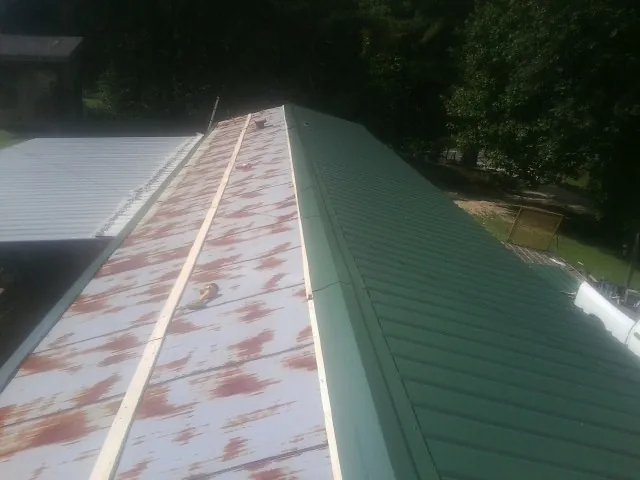 Old rusted panels beside newly installed green metal roofing — Wind Damage Roof Repair by Roofing Brothers in Sagle