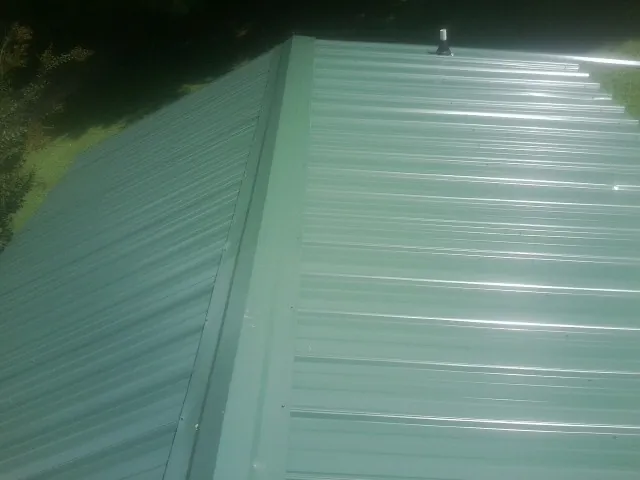 New green metal panels meeting at the ridge of a roof — Flat Roof Repair work by our crew in Sagle