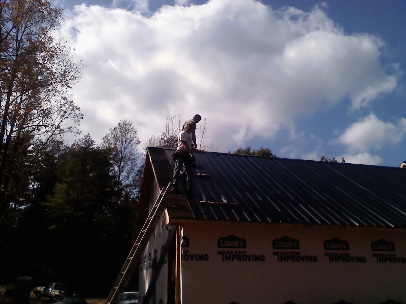 Roofer fastening dark metal panels high against a cloudy sky, from a Roof Inspection job in Sagle